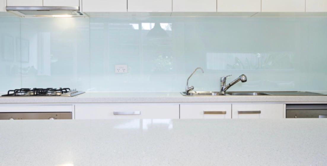 Modern kitchen with a clean white countertop, built-in gas stove, sink with faucet, and light blue glass backsplash. Cabinets and drawers are visible below the counter.
