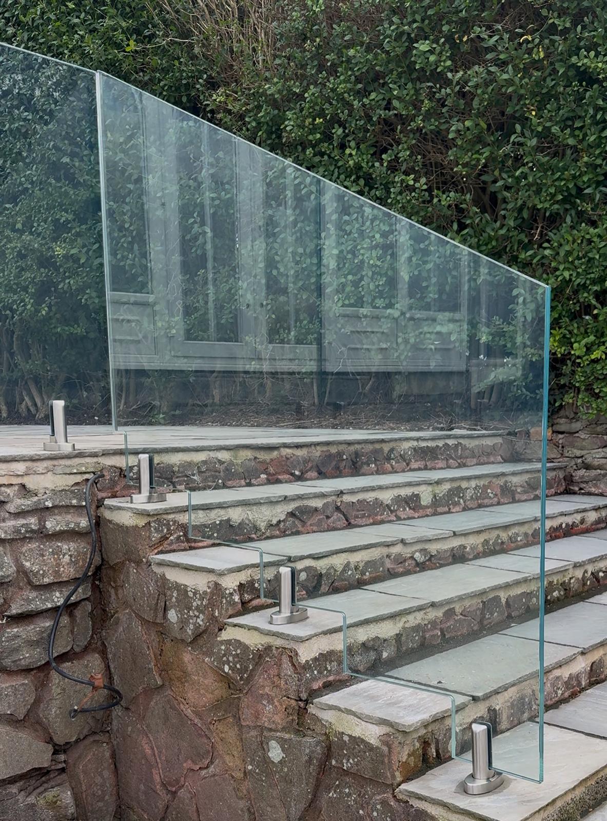 A glass balustrade with metal supports lines the edge of stone steps, blending into the background greenery and making the transparent barrier nearly invisible.
